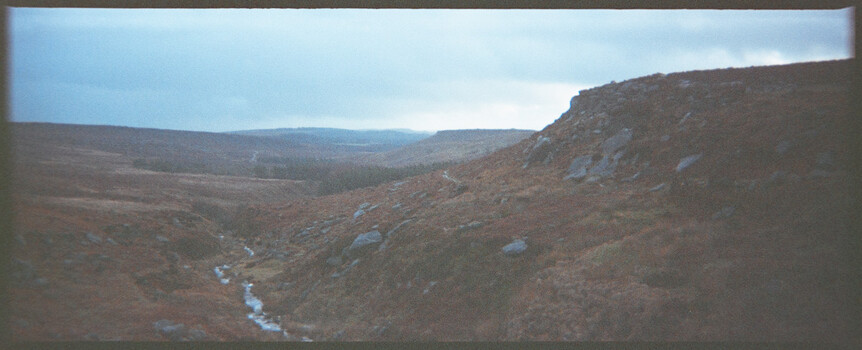 Highland valley landscape with stream flowing through moorland and distant forested slopes.