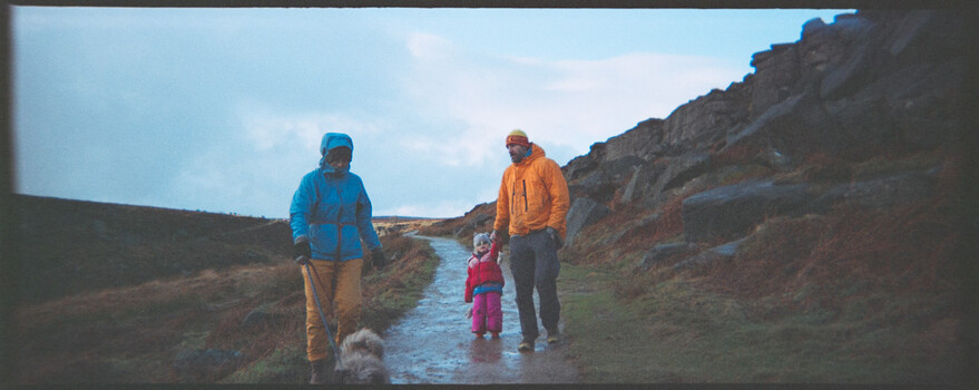 Three hikers walking through a shallow stream in a moorland valley on a clear day.