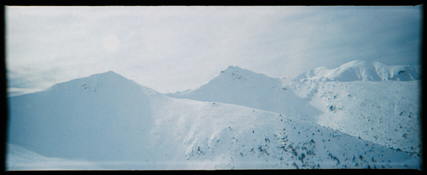 Snow-covered mountain peaks with sparse vegetation under clear sky.