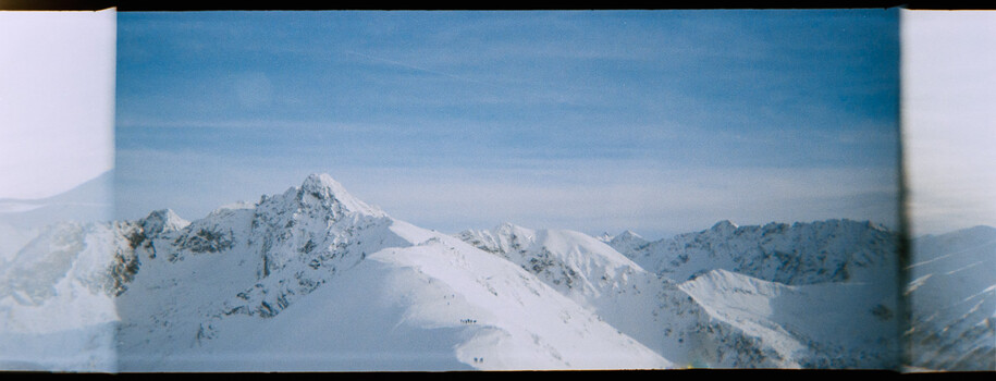 Snow-covered mountain peaks with exposed rock faces under clear blue sky.