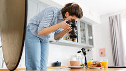 Photographer hunched over a table using a DSLR camera to shoot a food styling setup.