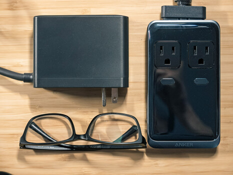 Travel power adapter kit with wall charger, power strip, and glasses on wooden surface.